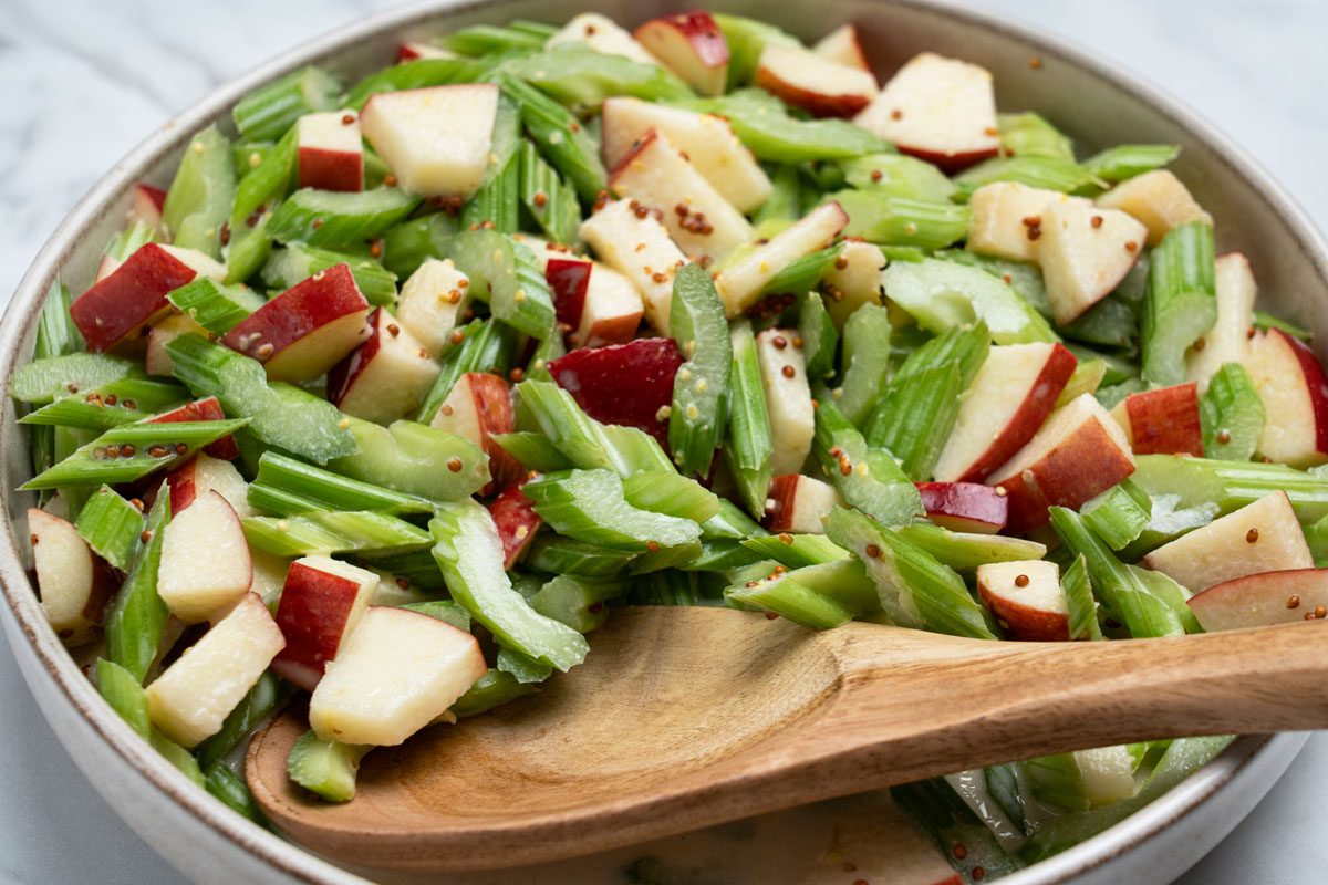 Closeup shot of Apple-Celery Salad in a large bowl with a wooden serving spoon; all set on a marble surface;