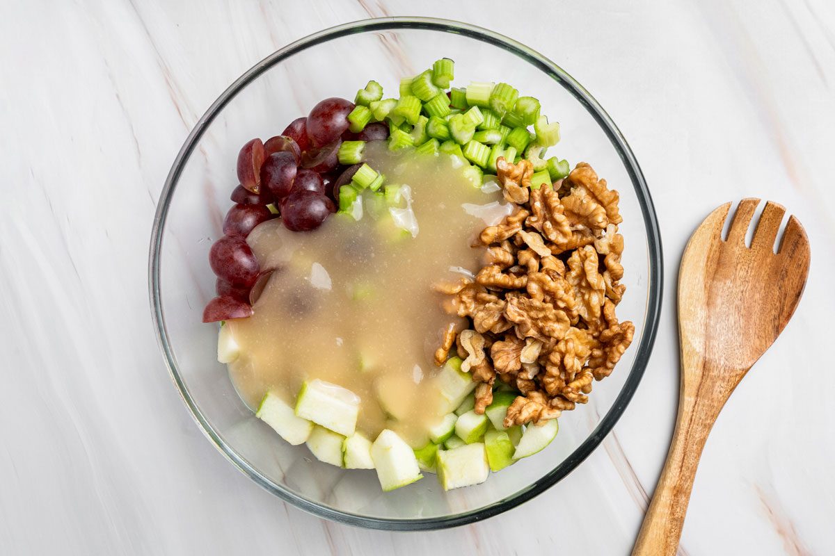 Overhead shot of add the dressing over combined mixtures; a wood spoon nearby; all set on a marble surface;