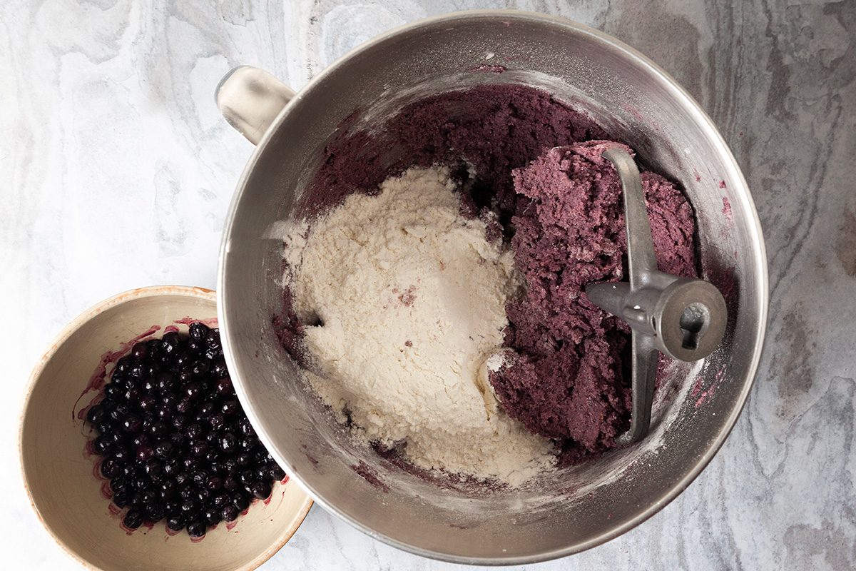 Overhead shot of small bowls; combine flour; baking powder and salt; add to the creamed mixture; beat on medium to low speed until just incorporated; fold in thawed wild blueberries; with juice; until incorporated; cover; refrigerate at least 2 hours; preheat oven to 400 degree; lace sugar in a shallow bowl; place confectioners sugar in a separate shallow bowl; scoop a rounded tablespoonful of the dough; gently roll into a ball; roll in sugar, then confectioners sugar; place on the baking sheet; repeat with remaining dough; spacing about 2 in; apart; all set on a marble surface;