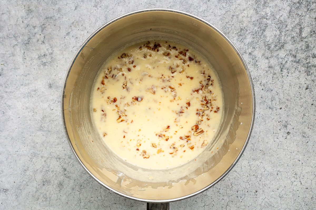 A metal saucepan containing a creamy sauce with visible specks of cooked bacon, sitting on a light gray textured surface.