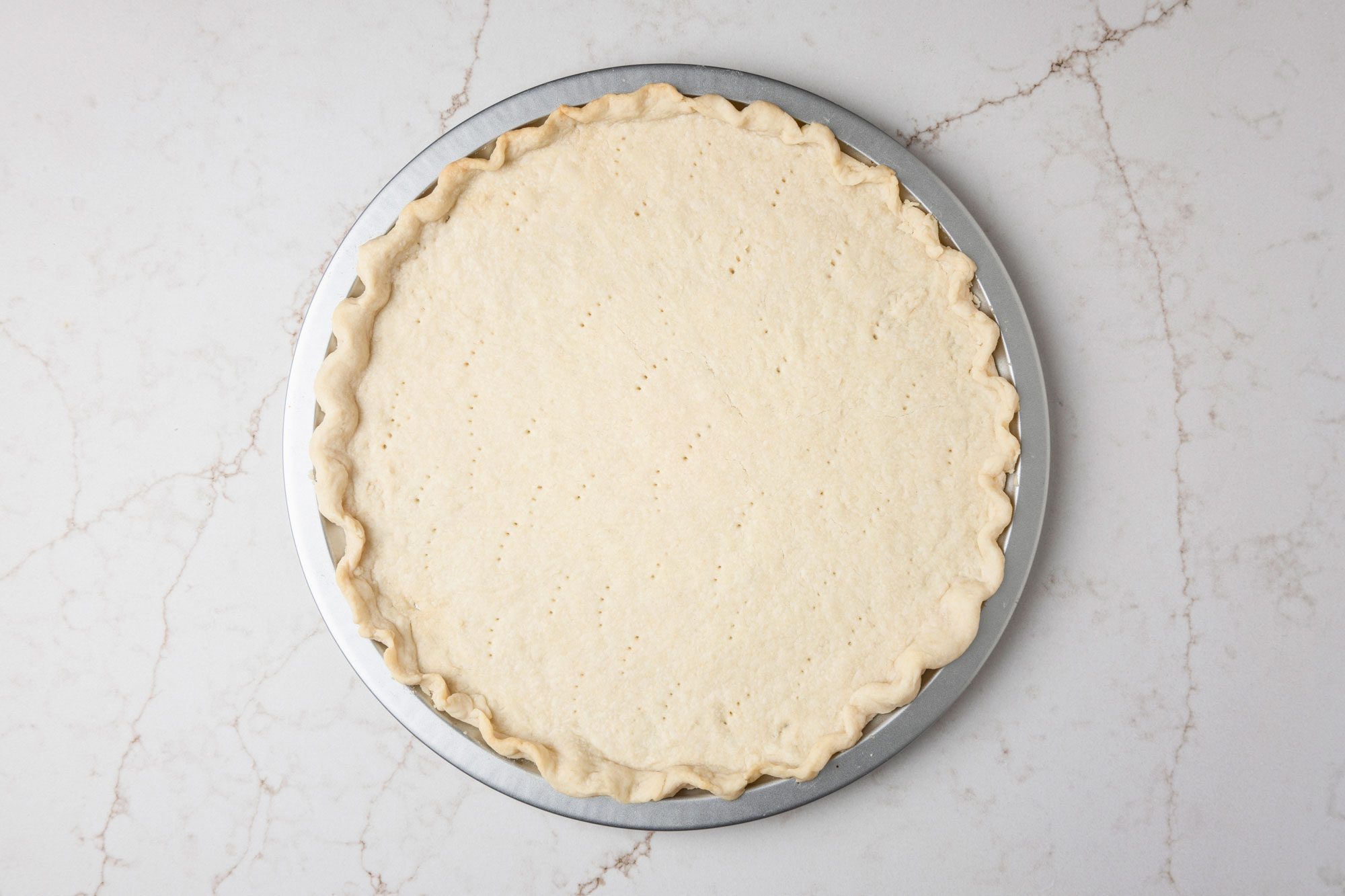 Overhead shot of roll out into a 14 inch circle; Place on an ungreased 12 inch pizza pan; Flute edges to form a rim; prick bottom of crust; Bake at 350 degree for 15 minutes; all set on a white texture marble surface