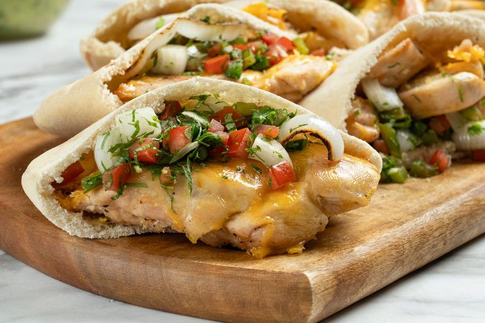 Pita bread filled with grilled chicken, melted cheese, diced tomatoes, onions, and fresh herbs, served on a wooden cutting board.