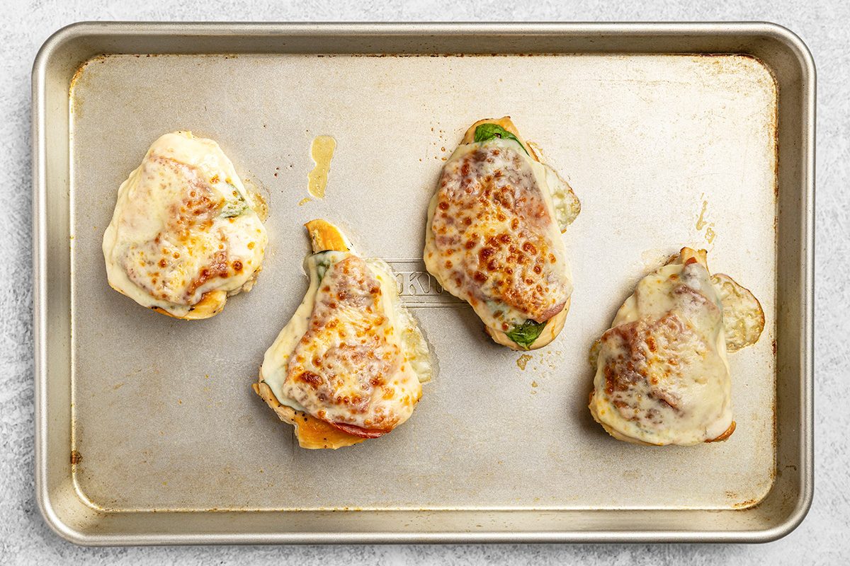 Four pieces of cooked chicken topped with melted cheese and possibly spinach or herbs, arranged on a metal baking sheet.