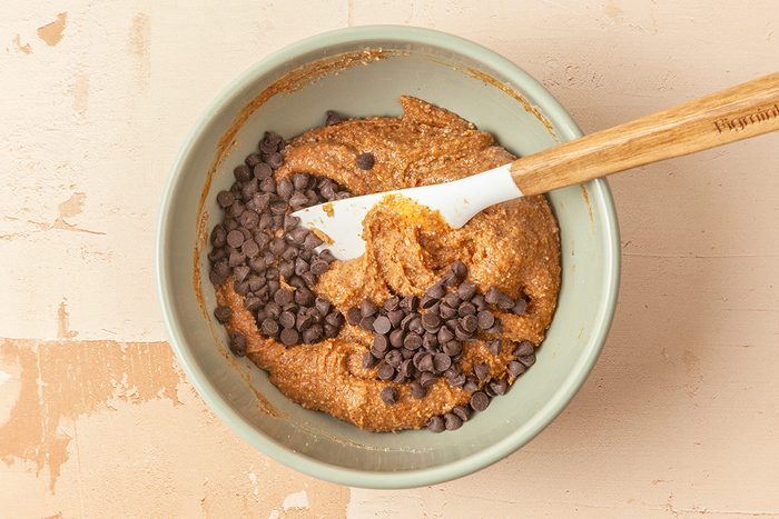 Overhead shot fo the same bowl; fold in chocolate chips; spatula; all set on a light orange background;