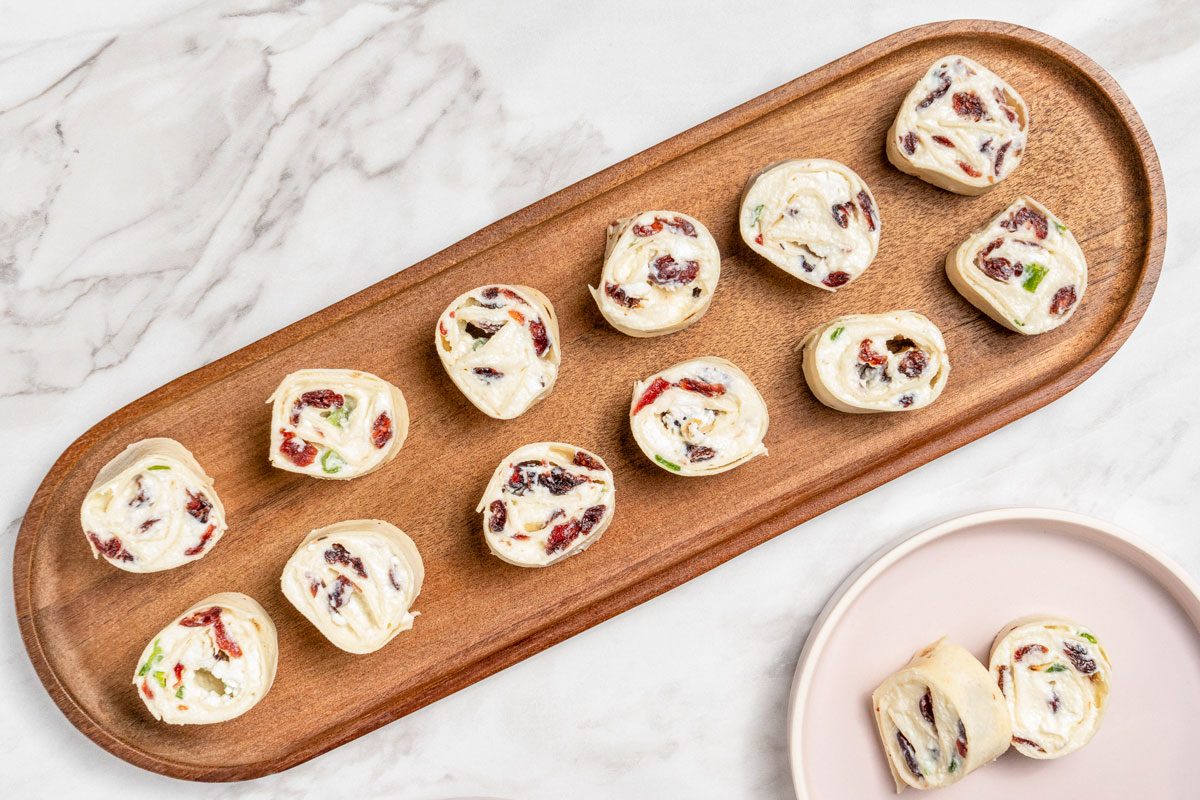 Overhead shot of Cranberry Feta Pinwheels placed on brown wooden platter; served on a small plate; all set on a white marble surface;