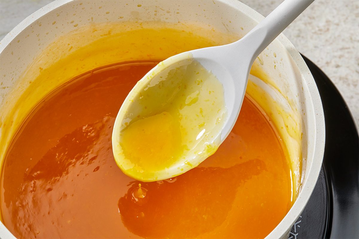 A white saucepan filled with bright orange and yellow melted sugar mixture, with a white spoon resting inside, coated in the thick, glossy liquid.