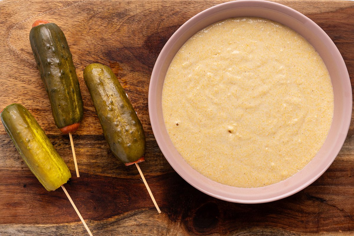 Batter is placed on the wooden table to dip the pickle hot dogs
