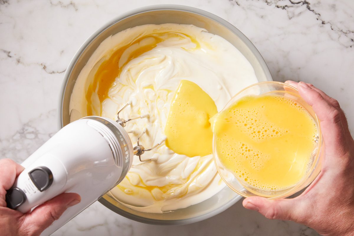 adding eggs to a mixture of cream cheese, sugar, sour cream, flour and vanilla