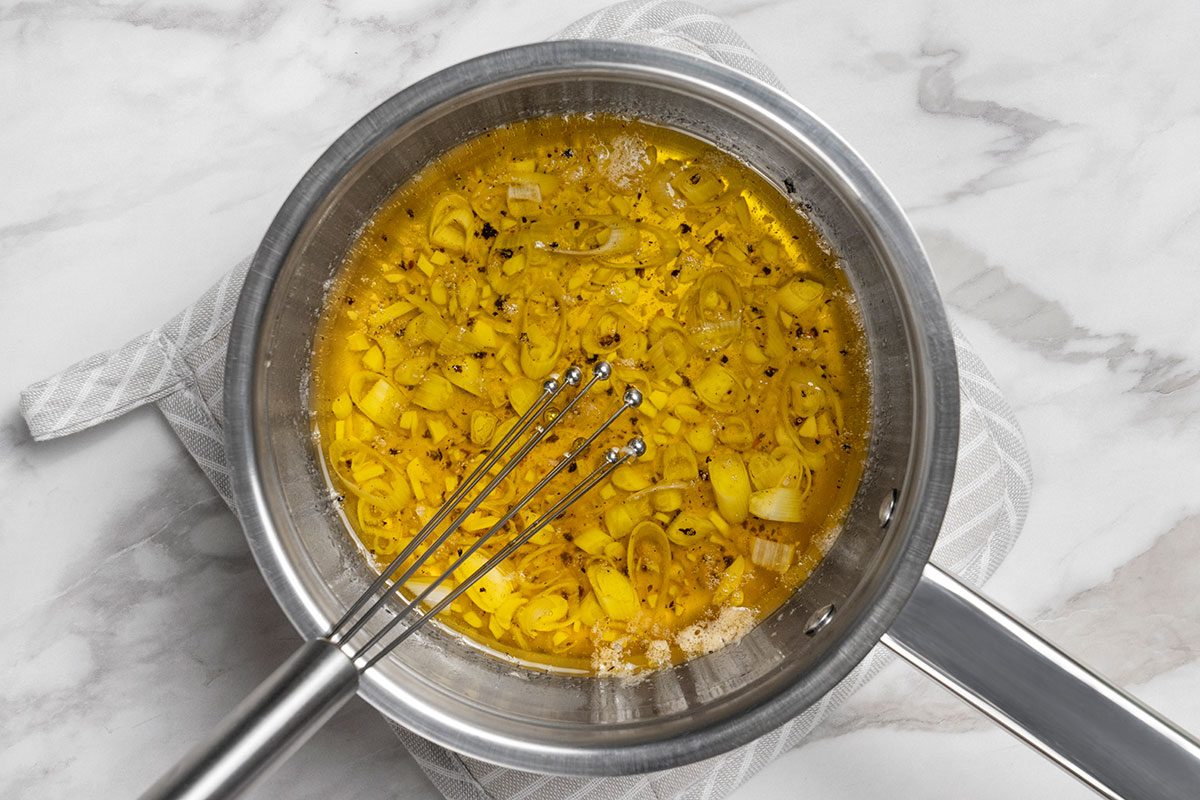 Oil, vinegar, onions, garlic, sugar, pepper and salt being whisked together in a small saucepan