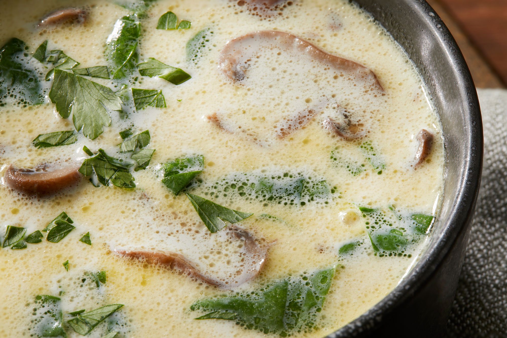 Close-up shot of Creamy Cremini-Spinach Soup served in a black bowl; sprinkled with parsley; placed over a grey napkin; all set on a brown wooden surface