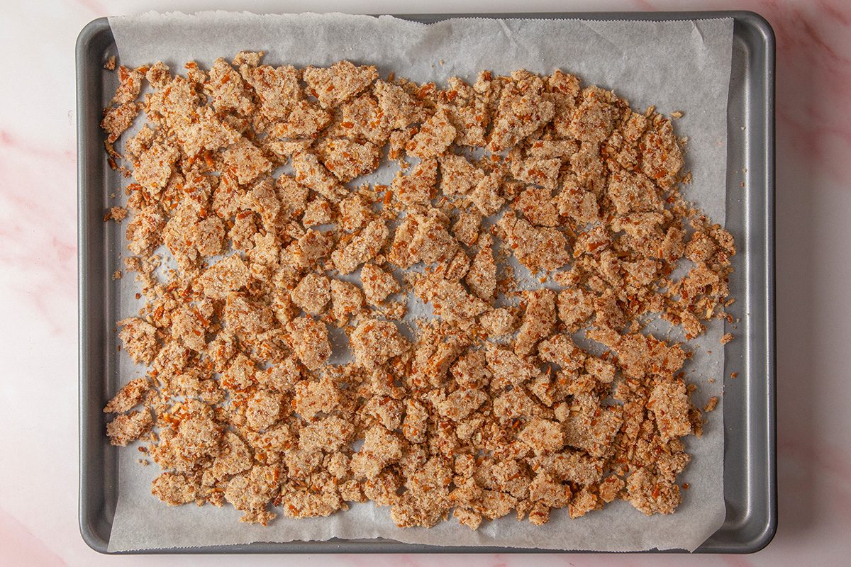 overhead shot of a baking sheet lined with parchment paper is covered with an even layer of crumbled, toasted brown bread pieces on a light pink marble surface