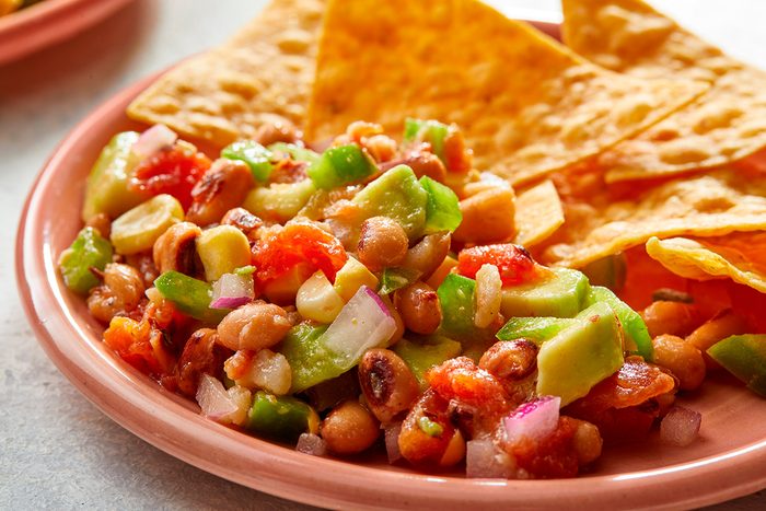 A plate with tortilla chips and a colorful bean salad made of black-eyed peas, avocado, tomatoes, green bell peppers, and onions.