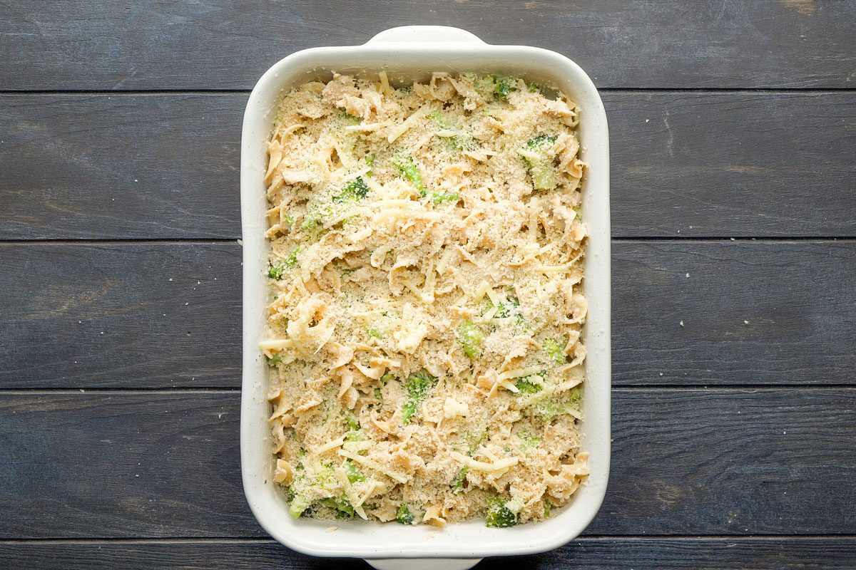 Top Shot of a white rectangular baking dish holds creamy pasta; broccoli; and shredded cheese, resting on a dark wooden surface; creating a delicious and inviting meal scene