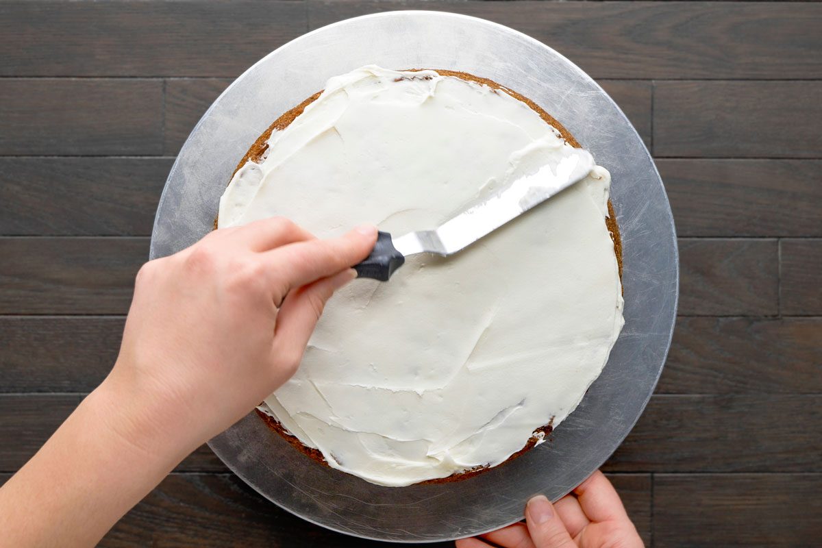 Overhead shot of spread between the layers and over the top and sides of the cake; cake knife; all set on a dark brown wooden surface;