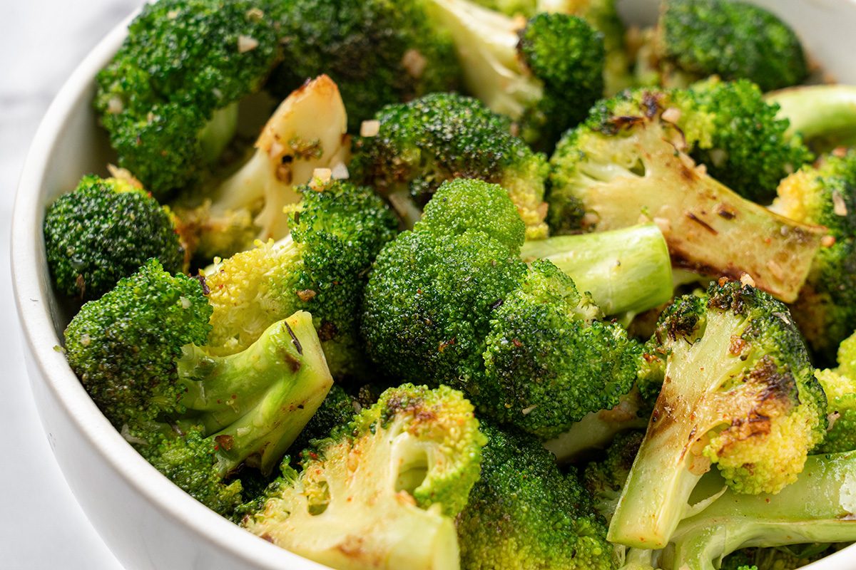 Close-up of a white bowl filled with roasted broccoli florets, featuring slightly browned edges and a light seasoning, giving the vegetables a vibrant green and golden appearance.