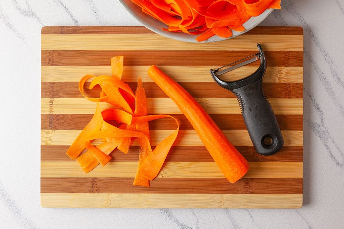 Peeled carror and peeler on a wooden chopping board