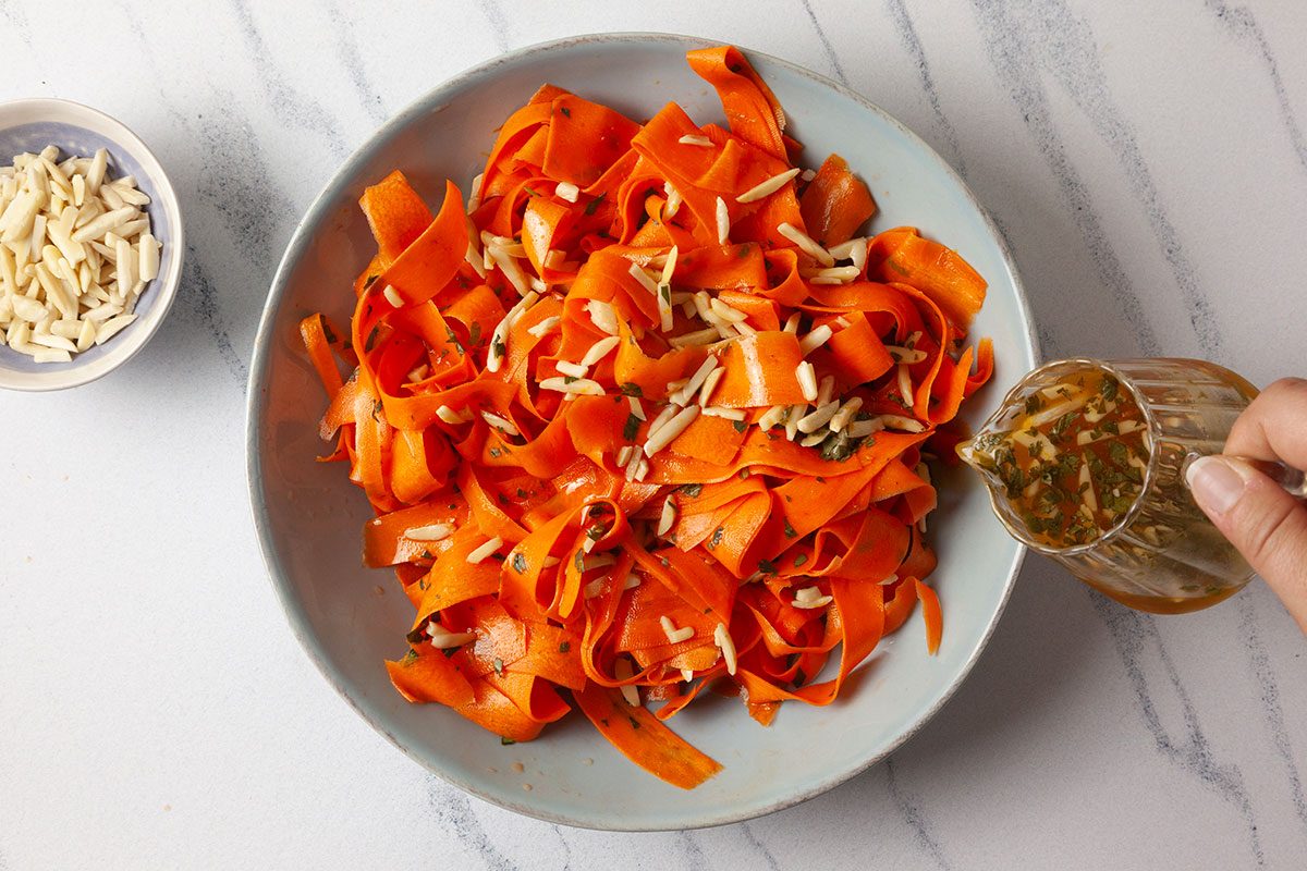 Salad dressing being poured on a carrot ribbon salad