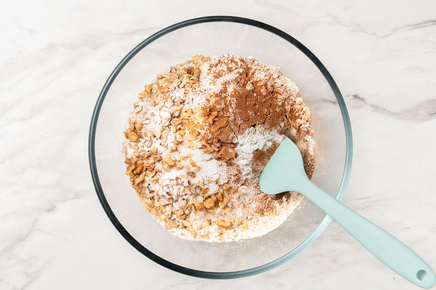 All-purpose flour, chopped nuts, ground cinnamon, baking soda, salt and baking powder combined in a glass bowl.