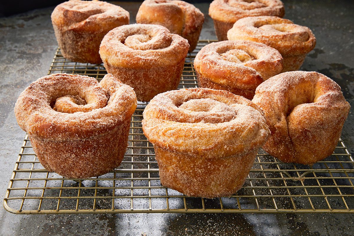 Close-up shot of Morning Buns cooling on a wire rack; their golden, swirled layers coated in sugar crystals against a dark surface;