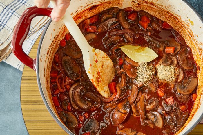 Overhead shot of dutch pot; stir in Worcestershire; bay leaf; thyme and rosemary; Simmer 8-10 minutes or until sauce is slightly reduced; spoon; induction; napkin; dark surface;