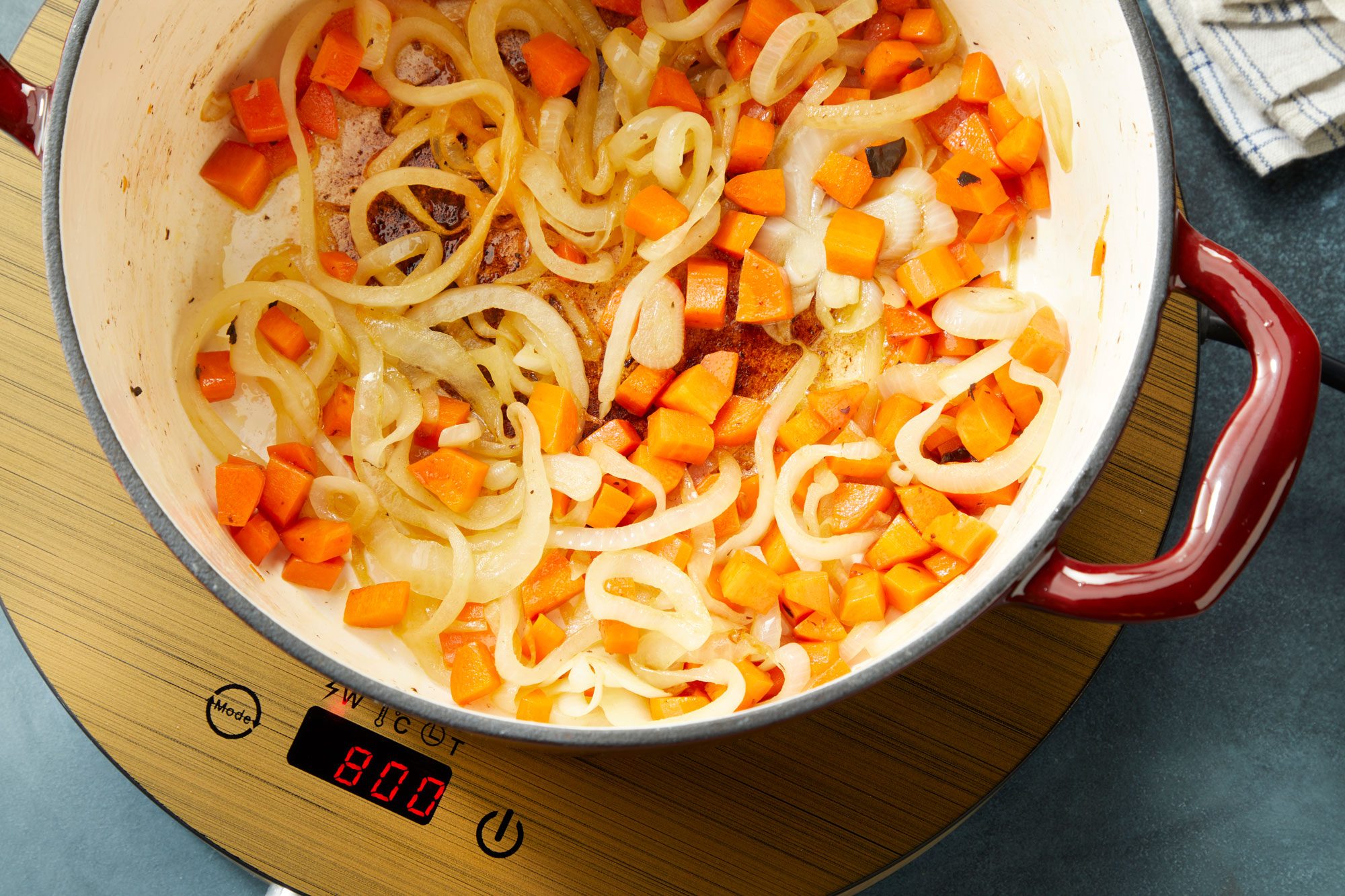 Overhaed shot of add remaining 2 tablespoons butter to Dutch oven; reduce heat to medium; add onion and carrot; cook until tender 6-8 minutes; induction; napkin; dark surface;