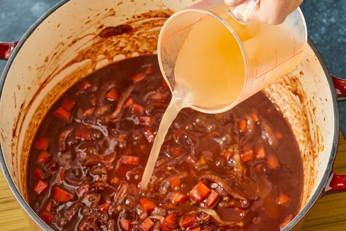 Close-up shot of stir in vegetable broth; bring to a simmer; induction; dark surface;