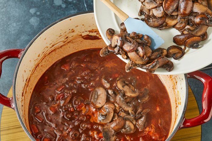 Overhead shot of add mushrooms back to the pot; induction; spatula; dark surface;