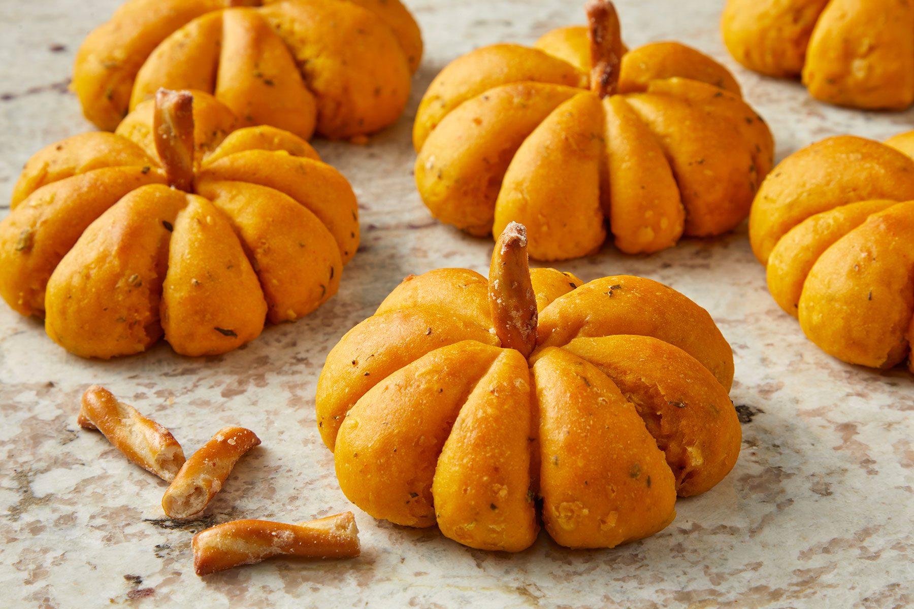 Golden pumpkin shaped rolls with inserted pretzel halves onto the top of each roll.