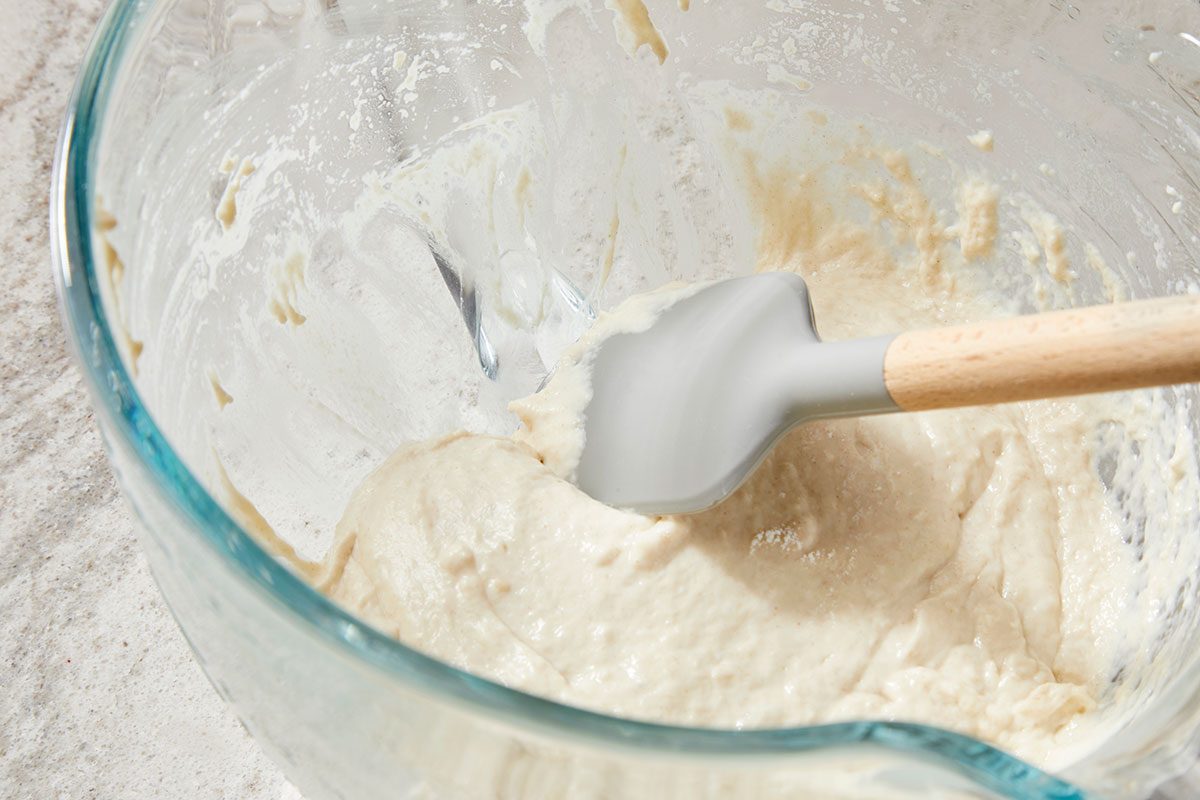 Overhead shot of a glass bowl filled with thick, creamy batter; with a silicone spatula resting inside; streaks of batter cling to the sides of the bowl; set on a light-colored surface. 