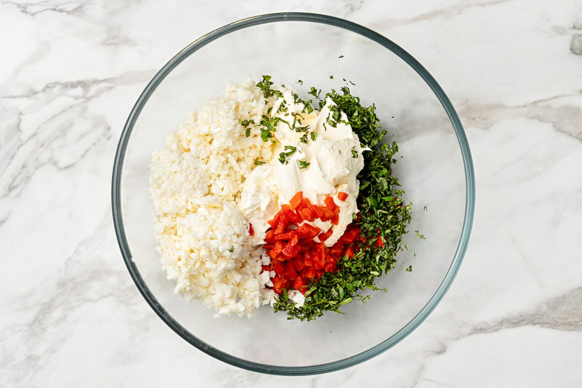 cream cheese, feta cheese, red peppers and basil in a bowl
