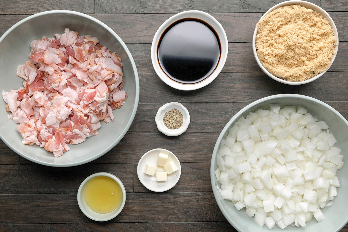 Bowls containing chopped bacon, diced onions, brown sugar, soy sauce, and a dish with cubes of butter, a small bowl of black pepper, and a bowl of oil, all arranged on a wooden surface.