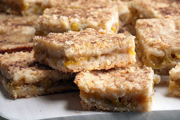A close-up of crumbly dessert bars stacked on a plate, featuring a golden-brown crust and visible filling, likely made with fruit or a similar sweet filling.