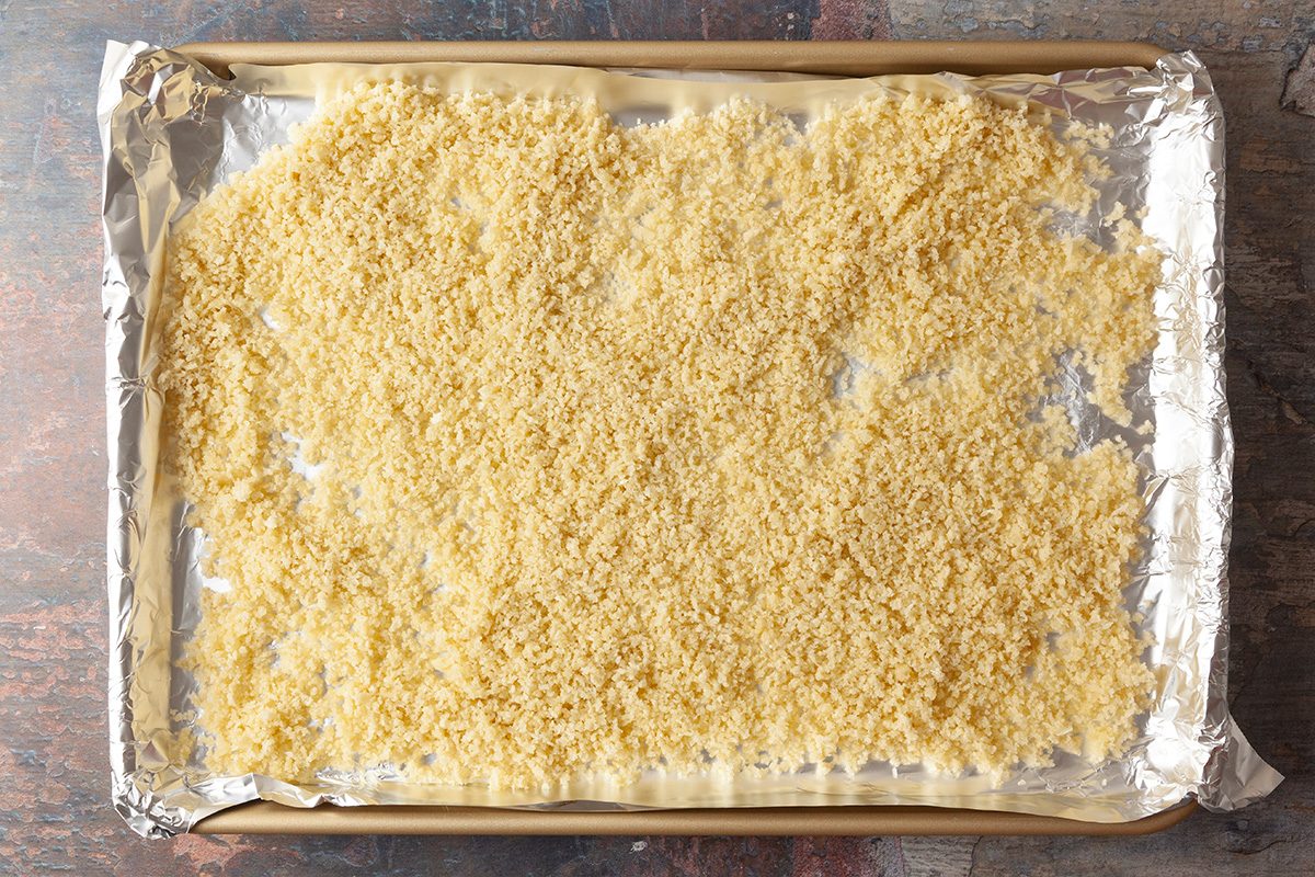 A baking sheet lined with foil is covered with an even layer of uncooked orzo pasta spread out across the surface.