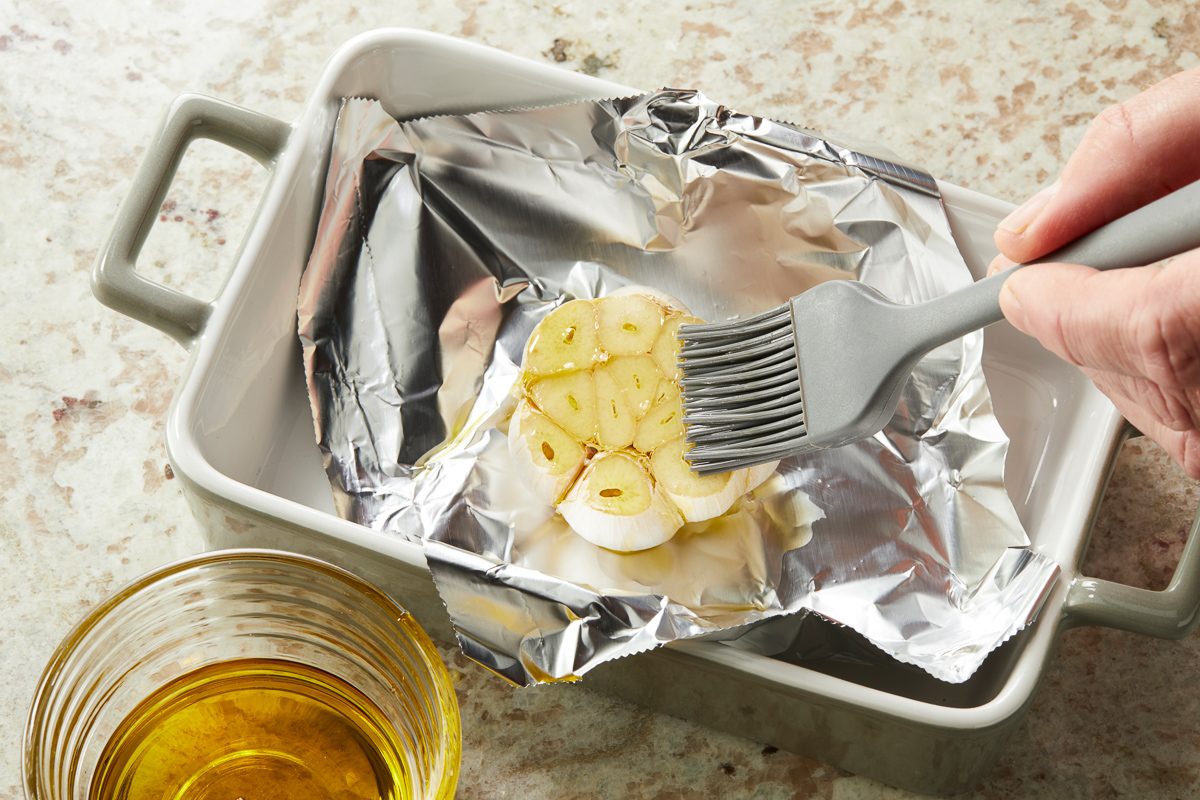 garlic bulb in foil being brushed with oil