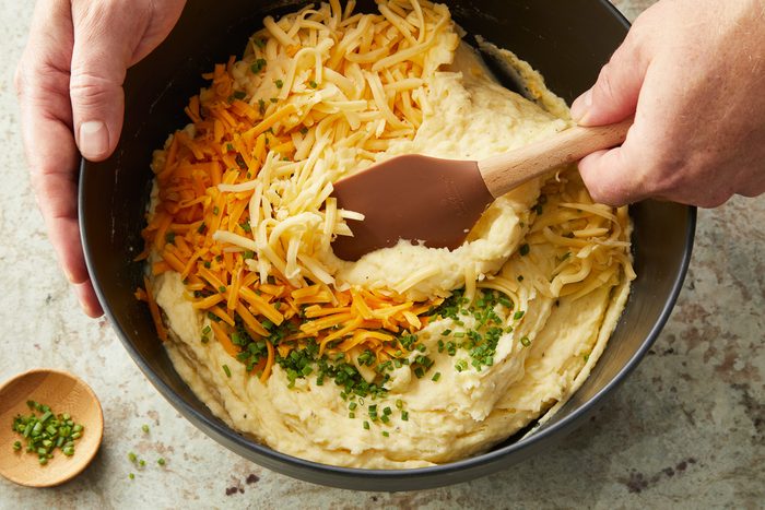 Gouda and cheddar cheese and the chives being stirred in with mashed potatoes