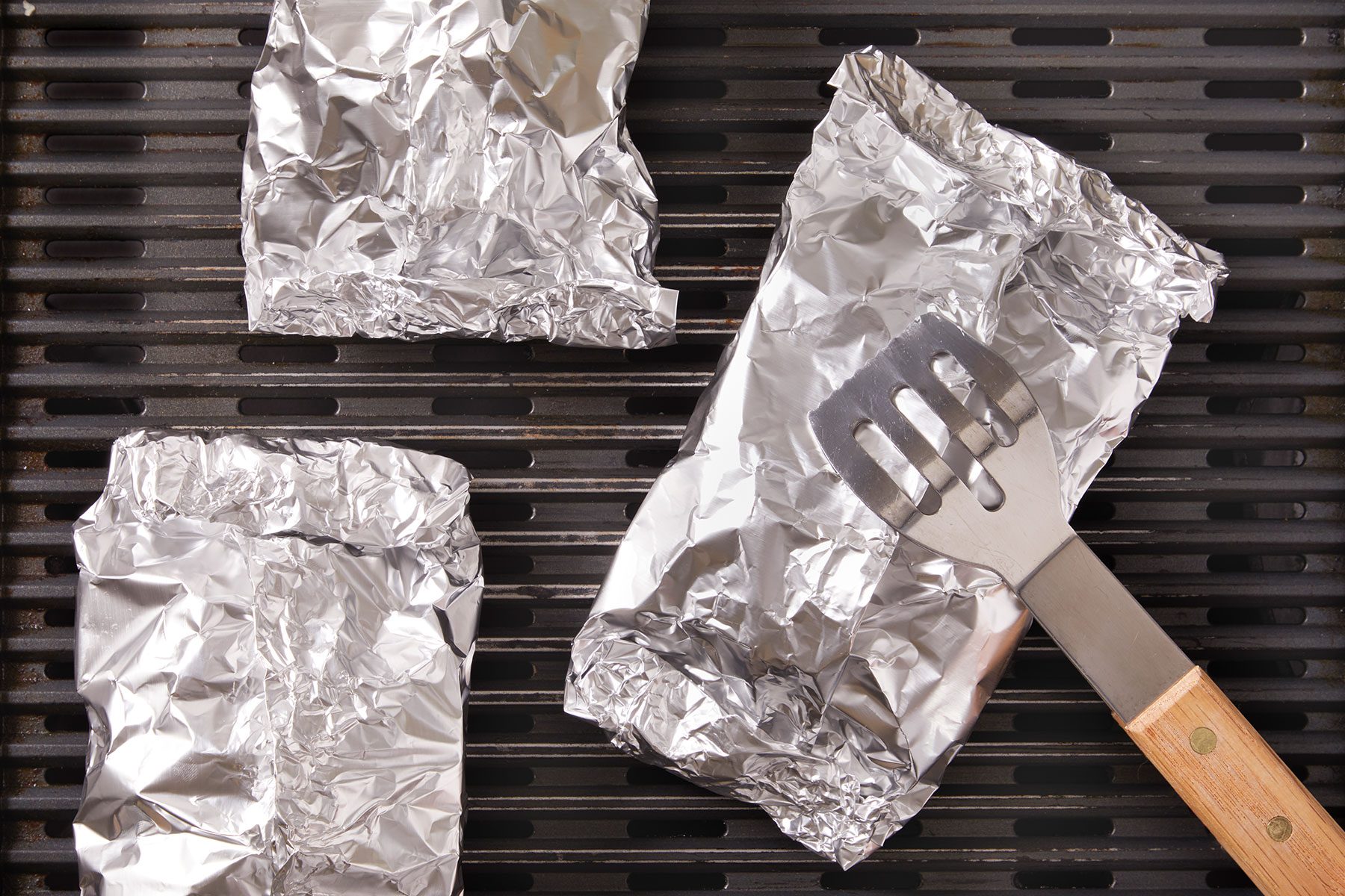 Steak And Potato Foil packets on the grill with a tossing laddle.