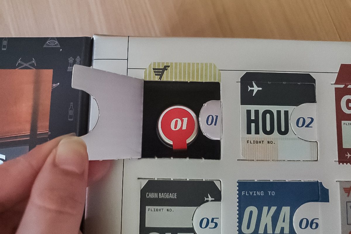 A hand is opening a flap labeled "01" on an advent calendar with an airline ticket theme. Other tickets with flight numbers and destinations are visible.