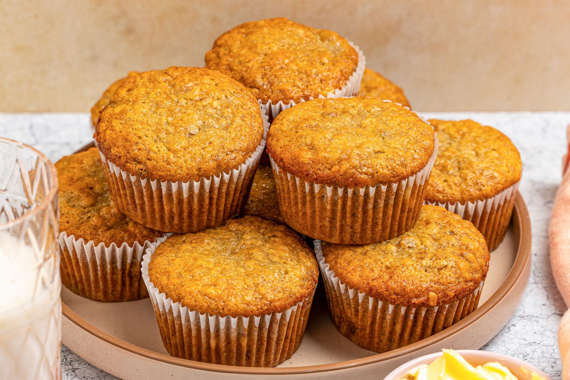 Close-up shot of vegan banana muffins stacked on a round tray; each in a white paper liner; placed on a gray surface