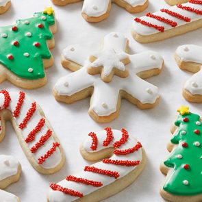 Assorted Christmas sugar cookies decorated with icing: green Christmas trees, white snowflakes, and red-striped candy canes arranged on a white surface.