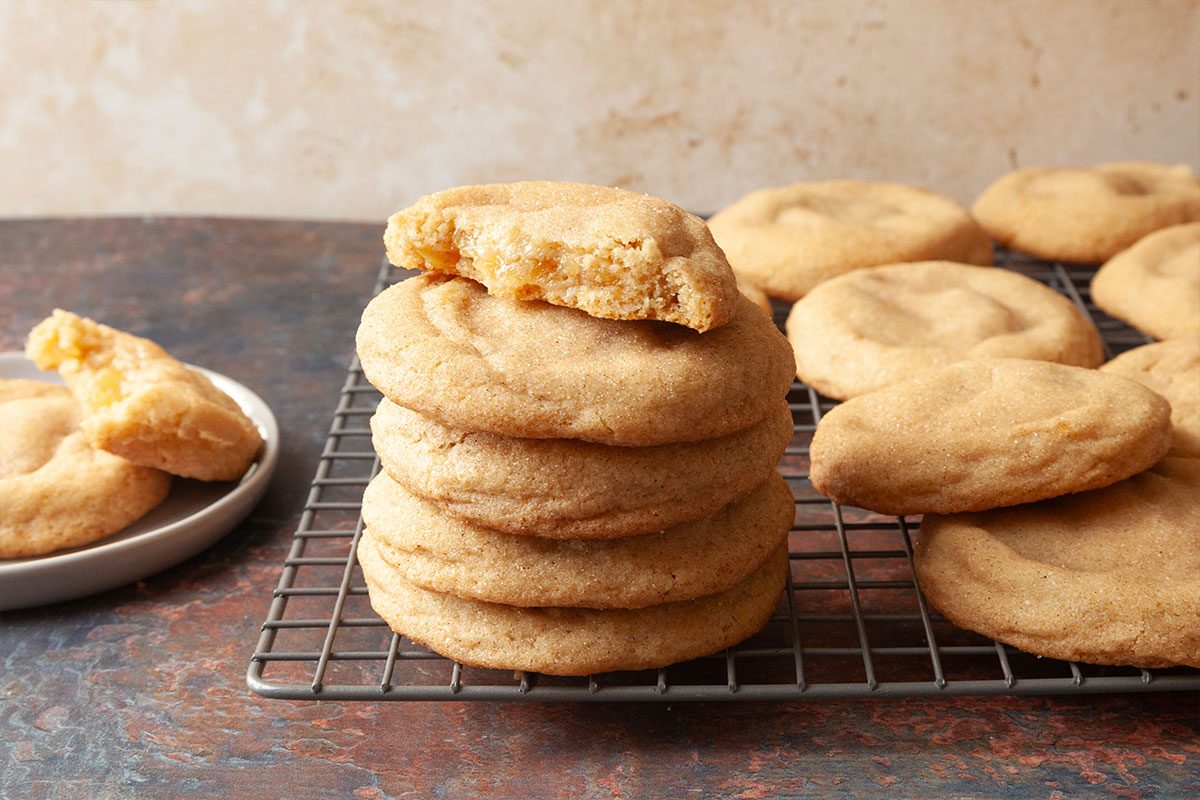 Close-up shot of a stack of Apple Pie-Stuffed Cookies on a cooling rack, with the top cookie bitten to reveal its soft filling and more cookies nearby