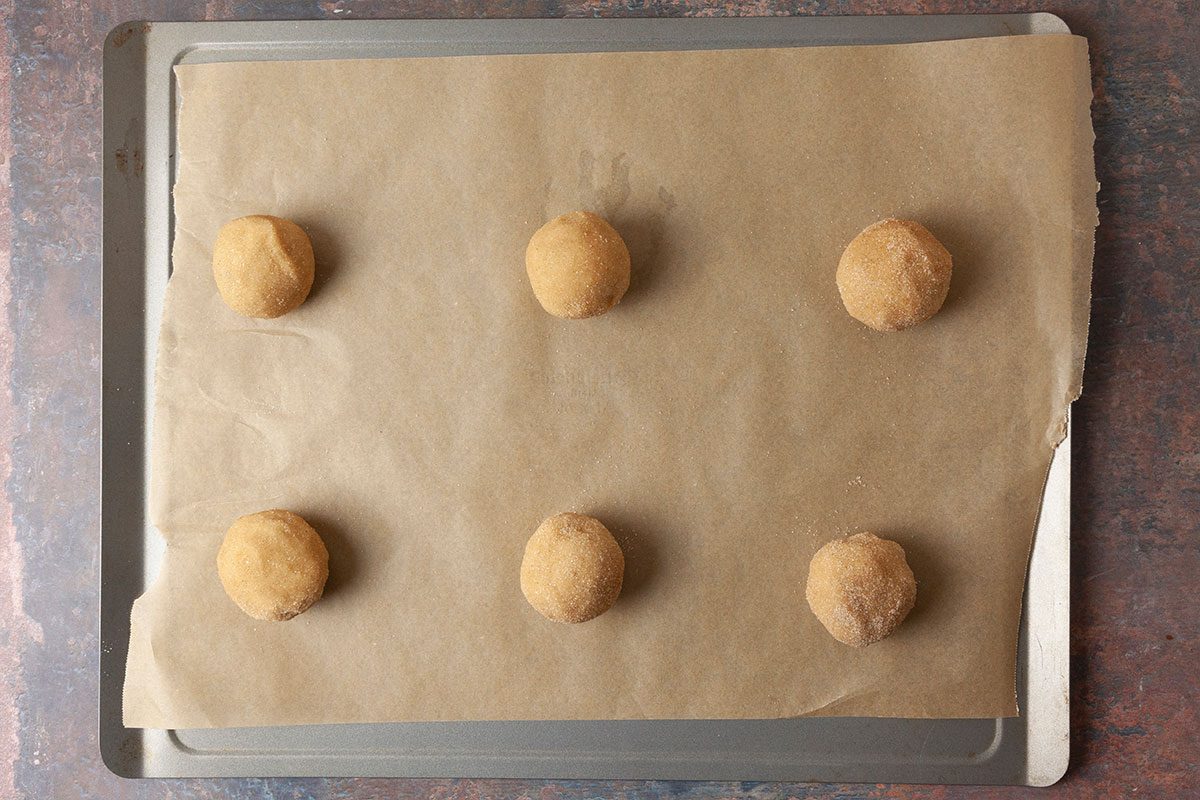 Overhead shot of a baking tray lined with parchment paper holding six evenly spaced, unbaked cookie dough balls ready for baking