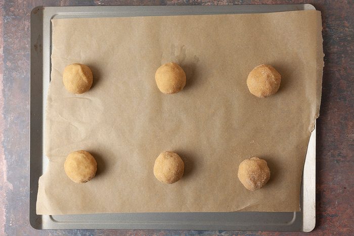 Overhead shot of a baking tray lined with parchment paper holding six evenly spaced, unbaked cookie dough balls ready for baking