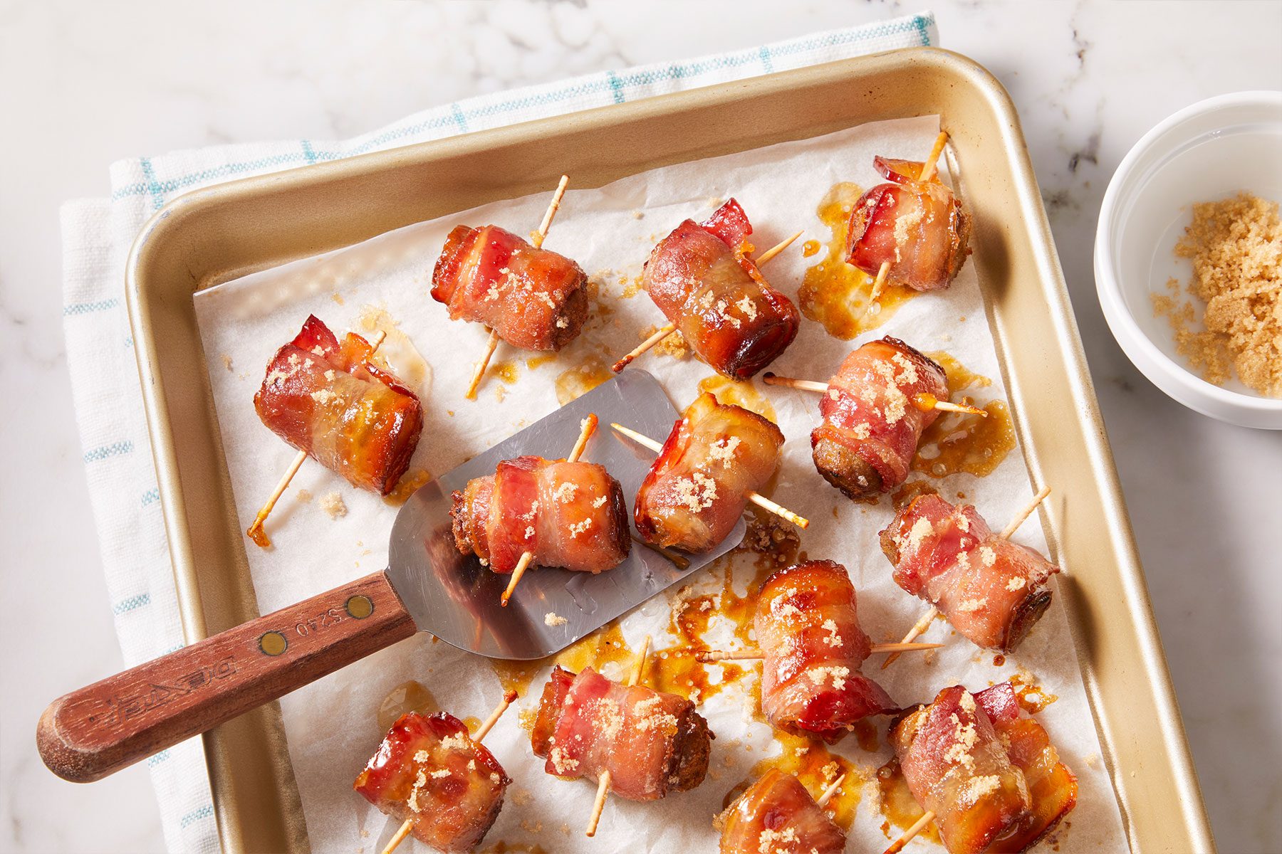 Baked Bacon Wrapped Sausage Bites in a tray with a serving ladle.