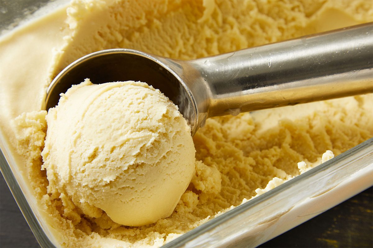 A closeup shot of a metal ice cream scoop lifting a round scoop of Bourbon ice cream from a glass dish filled with more ice cream