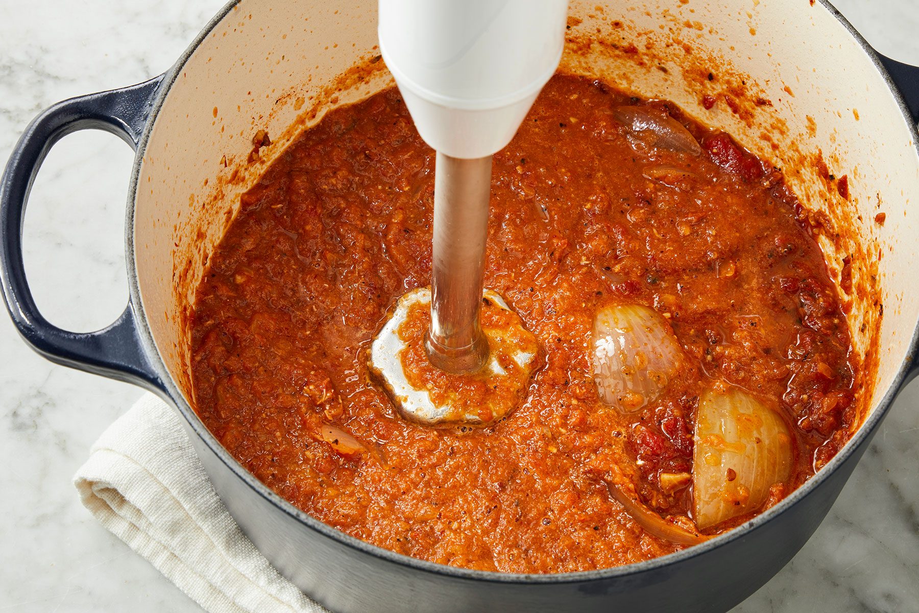 Using an immersion blender, pureeing the liquid in the pan mixture to make Chicken Tinga Tacos.