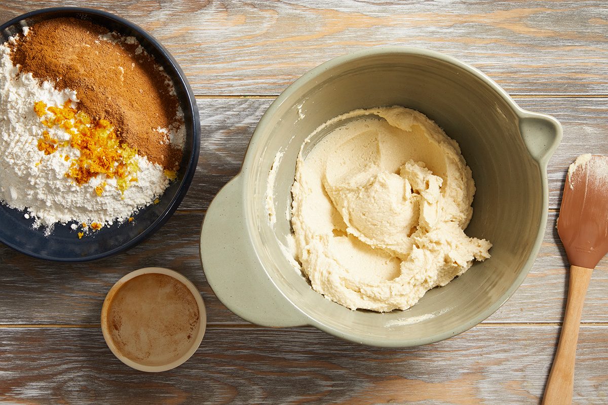 Overhead shot of butter and sugar mixture in a mixing bowl with a separate bowl of eggs and vanilla to the side, showcasing the creaming process.