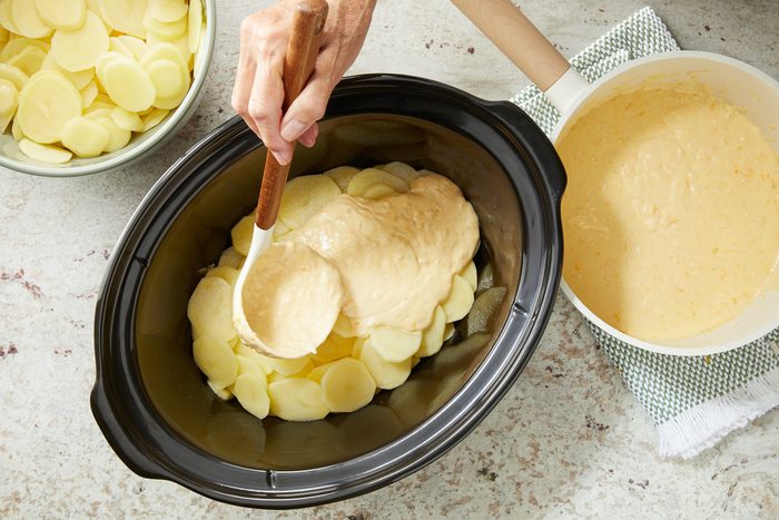 cheese mixture being poured over layer of potatoes