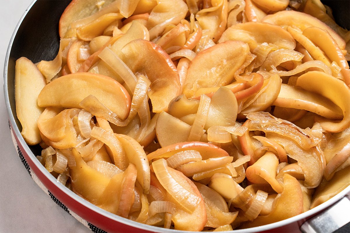 Close up shot of Fried Onions and Apples in the skillet; all set on a white marble surface;