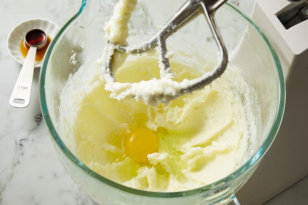 Overhead shot of butter and sugar being creamed together in a glass mixing bowl with electric beaters.