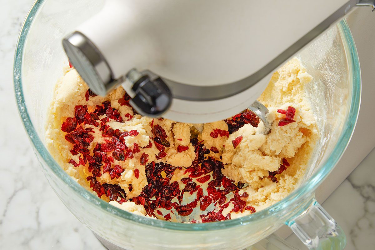 Overhead shot of chopped dried cranberries being stirred into cookie dough in a glass bowl.